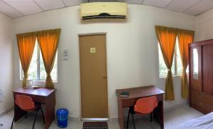a bedroom with two desks and a bed with orange curtains at Railway Hostel in Batu Gajah