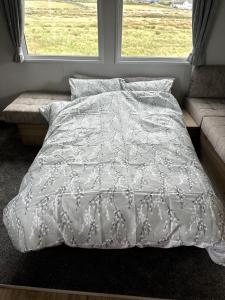 a bed with a white comforter and two windows at Luxury static caravan on SunnySands with mountain views in Barmouth
