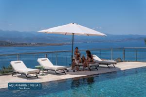 three women sitting under an umbrella next to a swimming pool at Seacrete villas in Chania