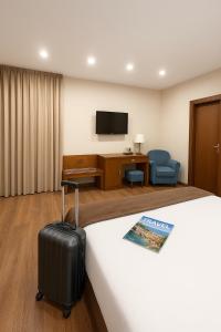 una stanza d'albergo con un letto con una valigia e una tv di Hotel Palace Sevilla a Siviglia