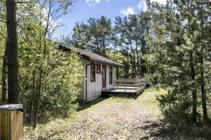a small white cabin in the woods with a porch at 1322-Aakirkeby-Malurtvej-10 in Vester Sømarken