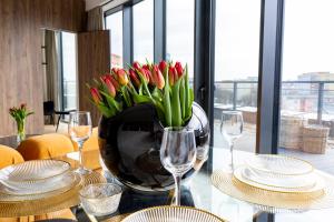 Un jarrón de tulipanes rojos sobre una mesa con vasos. en Kaleo apartments - Hanza Tower 605, en Szczecin