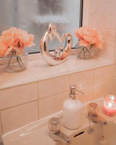 a bathroom sink with two vases with pink flowers at Lovely 2 Bedroom Home Coventry in Tollbar End