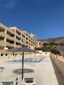 a pool with chairs and an umbrella in front of a building at Costa Adeje Dream View - 2 Bedroom Apartment with Terrace in Adeje
