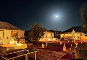un grupo de tiendas de campaña por la noche con la luna en Merzouga Desert Campsite &Activities, en Merzouga
