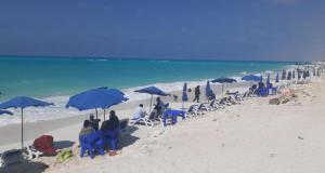 Un grupo de personas sentadas bajo sombrillas en una playa. en قرية أكوا فيو الساحل الشمالي - Aqua View El Alamein, en El Qasaba esh Sharqīya