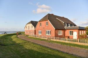 a red brick house with a fence next to the water at Hallig Hüs in Langeneß