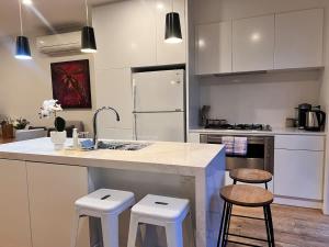 a kitchen with white cabinets and a counter with stools at Modern Port Melbourne 3b3b Townhouse and Parking in Melbourne