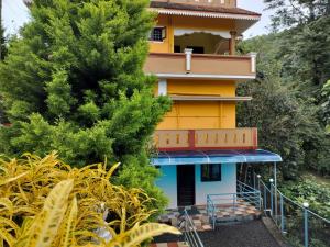 a yellow and blue building with a tree at Allora homestay in Vagamon