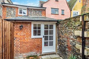 a brick house with a white door and a brick wall at Hawker Cottage in Lavenham