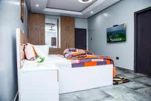 Cette chambre comprend un lit blanc et une télévision murale. dans l'établissement PEK Villa, Cozy Luxury Hideouts, 25 mins from Airport, à North Legon