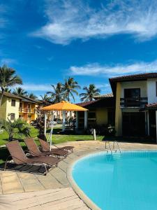 a swimming pool with two chairs and an umbrella at Apartamento Em frente a praia - Piscina condomínio América Praia, acesso privativo para a praia in Porto Seguro