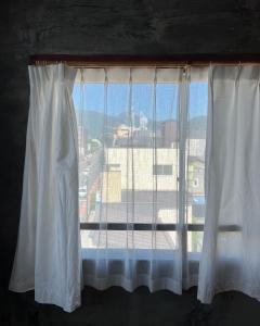 una ventana con cortinas blancas y vistas a la ciudad en めくる, en Matsumoto