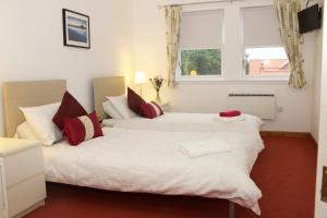 Duas camas num quarto com lençóis brancos e almofadas vermelhas em Pintail Apartment Bamburgh em Bamburgh