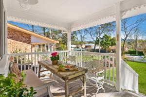 a white porch with a wooden table and chairs at Lady Rose Cottage Jamberoo in Jamberoo