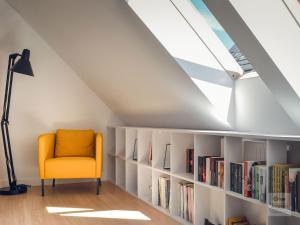 an attic room with a yellow chair and bookshelves at Ataner Apartamenty in Koszalin