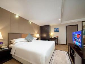 Un dormitorio con una gran cama blanca y un televisor de pantalla plana. en Zhuhai Aqueen Hotel, en Zhuhai