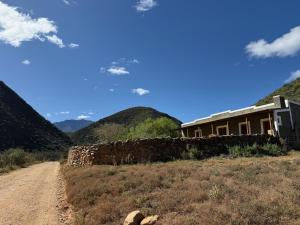 a house on a dirt road with mountains in the background at Klipkraal Cottage in Calitzdorp
