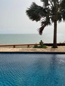 a swimming pool with a palm tree and the ocean at Maison Atlantique in Rufisque