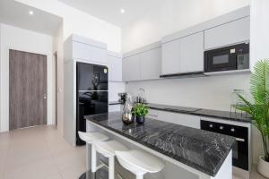a white kitchen with a black counter and stools at Luxury Modern Villa Phuket - Thala in Phuket