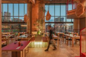 a person walking through a restaurant with tables and windows at Wake BioHotel, a Member of Design Hotels in Medellín