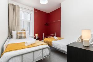 two beds in a room with red walls at The Maple Haven – Spacious 3BR with FREE Parking in Jarrow