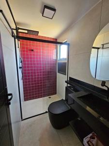 Un baño con ducha roja con inodoro y espejo. en Lofts 4 Elementos - Fogo - Martim de Sá - Caraguatatuba, en Caraguatatuba