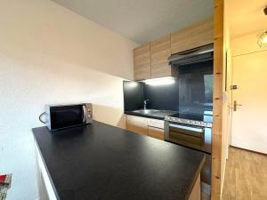 a kitchen with a black counter top with a microwave at Studio lumineux avec balcon, au pied des pistes, Les Menuires – 3 personnes - FR-1-452-17 in Les Menuires