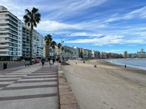 a beach with palm trees and buildings and people walking at Rambla Bliss Suites con Vista al Mar in Montevideo