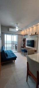 een woonkamer met een blauwe bank en een televisie bij Ape Condomínio Club - pé na areia in Mongaguá