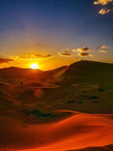 a sunset in the desert with the sun setting at Bafana Erg Camp Merzouga in Merzouga