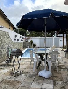 a table and chairs with a blue umbrella next to a pool at Casa de Praia Encanto Tamandaré - A 300m das Piscinas Naturais in Tamandaré