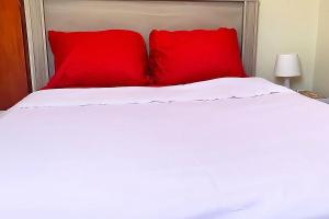 a white bed with two red pillows on it at Guest Favorite - Central - Gated - 2 Bedrooms in Willemstad