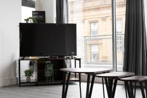 Una sala de estar con televisión y dos mesas y una gran ventana. en Buchanan Penthouse, en Glasgow