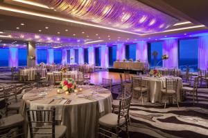 un salón de banquetes con mesas y sillas blancas e iluminación púrpura en The Westin Dallas Downtown, en Dallas
