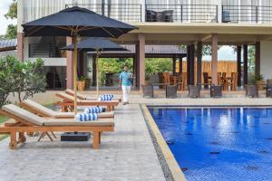 a person standing next to a swimming pool with chairs and umbrellas at Hotel Sigiriyaaya - Jetwing Select in Sigiriya
