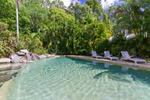 a swimming pool with two lounge chairs and trees at Port Douglas Plantation Resort in Port Douglas