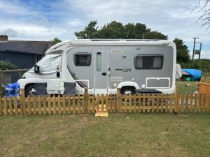 a grey caravan parked behind a wooden fence at Izzie The Glampervan in Faversham