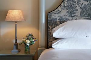 ein Bett mit einer Lampe und einer Vase mit Blumen auf einem Tisch in der Unterkunft Grey's Court Cottages in Southrop