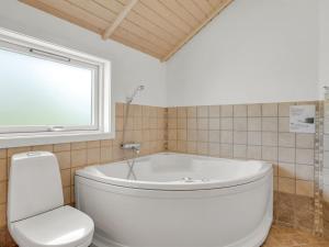 a white tub in a bathroom with a toilet and a window at Holiday Home Alger - 800m from the sea by Interhome in Marielyst