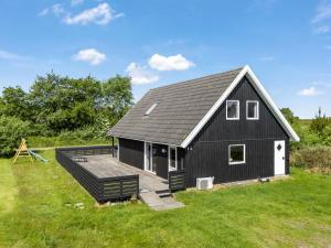 a black barn with a deck in a field at Holiday Home Sunita - 2-8km from the sea by Interhome in Toftum
