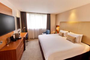 a hotel room with a large bed and a flat screen tv at Thistle London Hyde Park Kensington Gardens in London