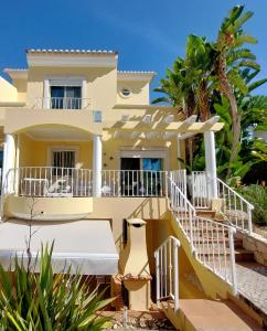 a yellow house with white railings and palm trees at Vilapeti by SAPvillas in Vilamoura