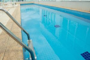 a blue swimming pool with a metal hand rail at Apartamento moderno e aconchegante com vista para a Esplanada in Brasília
