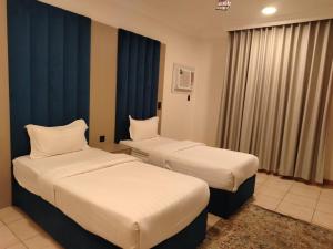 two beds in a hotel room with blue curtains at زهرة الضيوف شقق مفروشة in Dammam