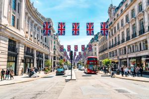 a red bus driving down a street with british flags at The Vanity Affair - Fitzrovia - By Frankie Says in London