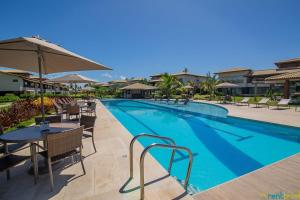 a swimming pool with tables and chairs and an umbrella at Ykutiba Imbassaí - Apartamento Superior - I104 in Imbassai