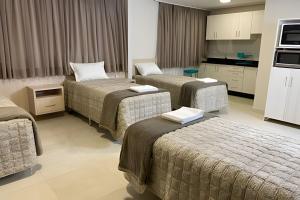 a hotel room with three beds and a kitchen at Edifício Shalfa in Foz do Iguaçu