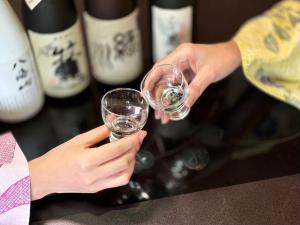 Dos personas sosteniendo copas de vino frente a botellas de vino. en Kutsurogian, en Minami Uonuma