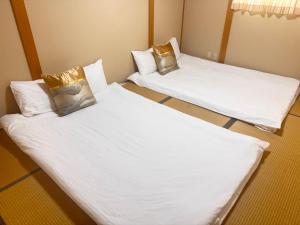 two beds in a room with white sheets and gold pillows at 谷町の宿 in Osaka